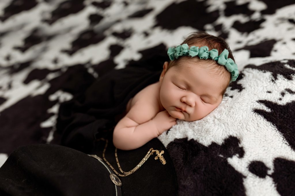 Newborn sleeping peacefully next to grandfather’s cowboy hat and belt in Iowa studio session.