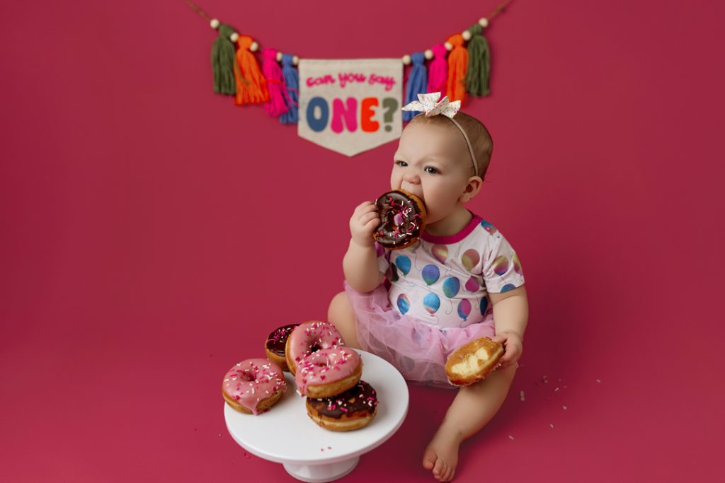 Baby girl enjoying donut-themed cake smash session near Waterloo, Iowa.