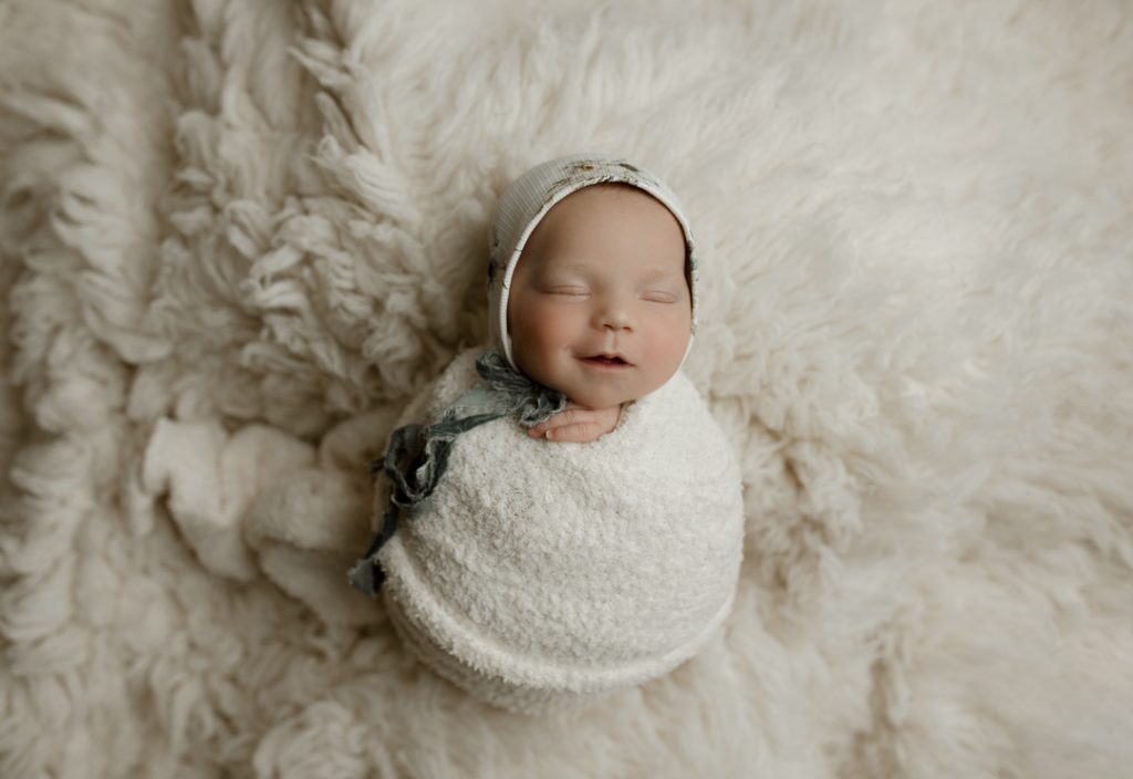 Smiling newborn in custom wrap and bonnet during Waterloo, IA newborn session.
