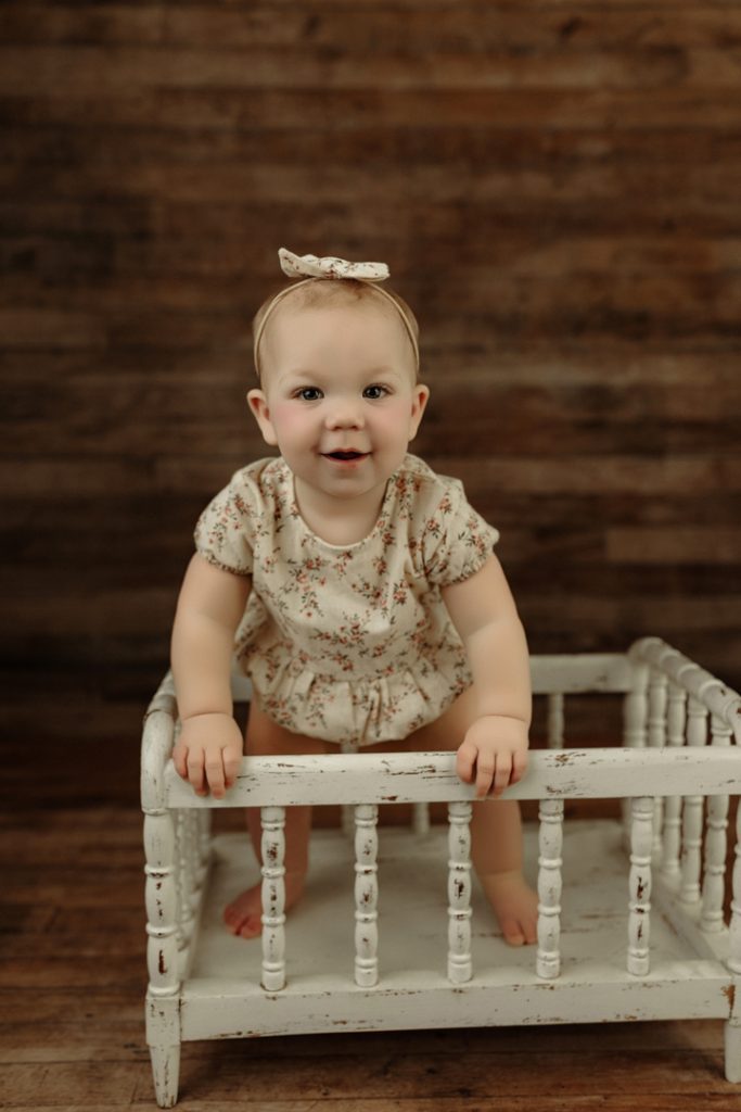 Adorable baby girl standing and smiling during milestone session near Waverly, IA.