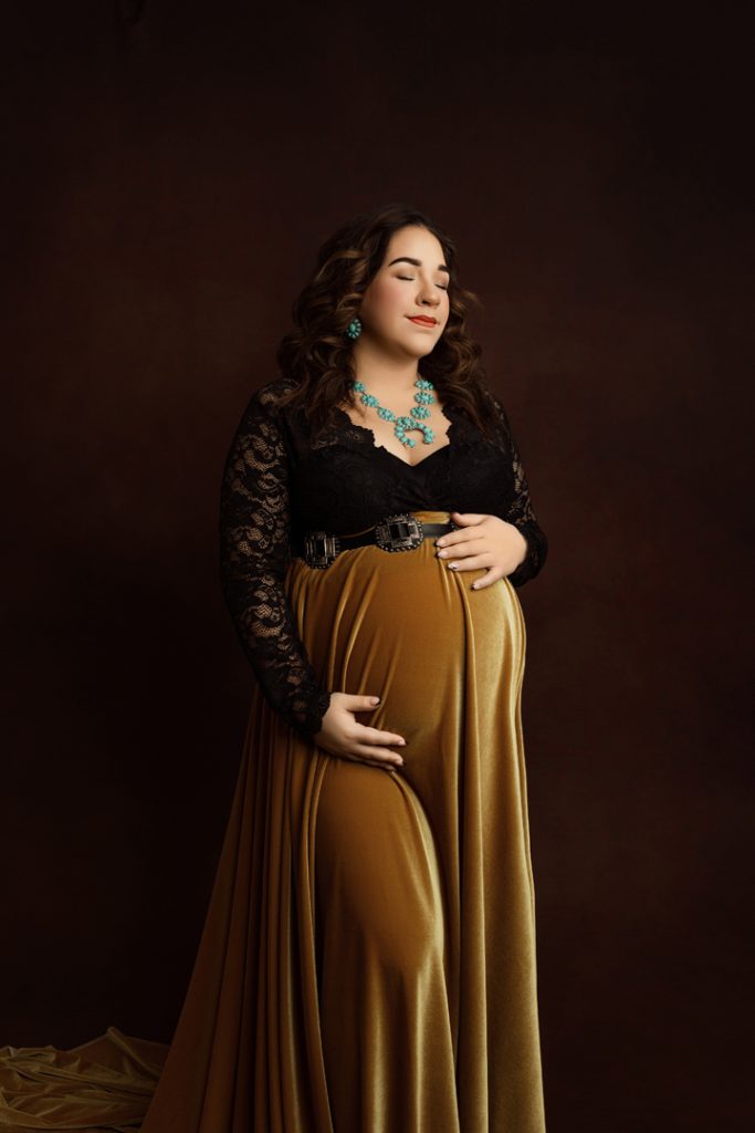 Expecting mother posing elegantly in a handmade golden velvet maternity gown near Waterloo, IA.