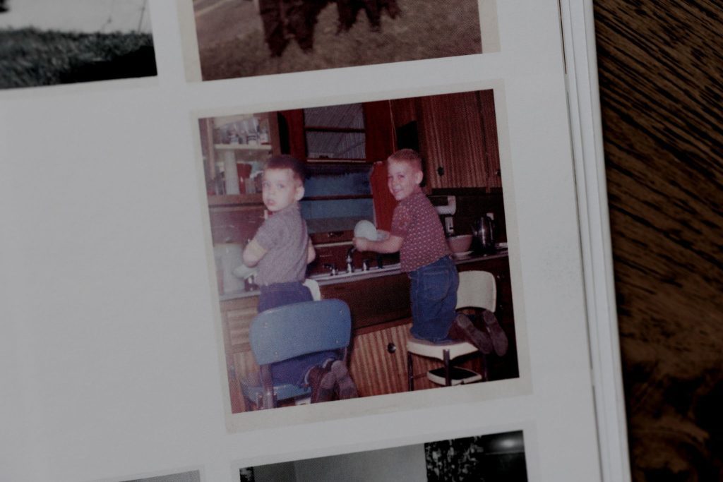 Two young boys doing dishes at the kitchen sink in a candid vintage photo.
