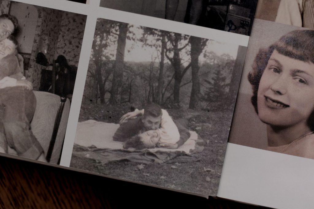 Black and white photo of a couple playfully laying together on a blanket in the woods.