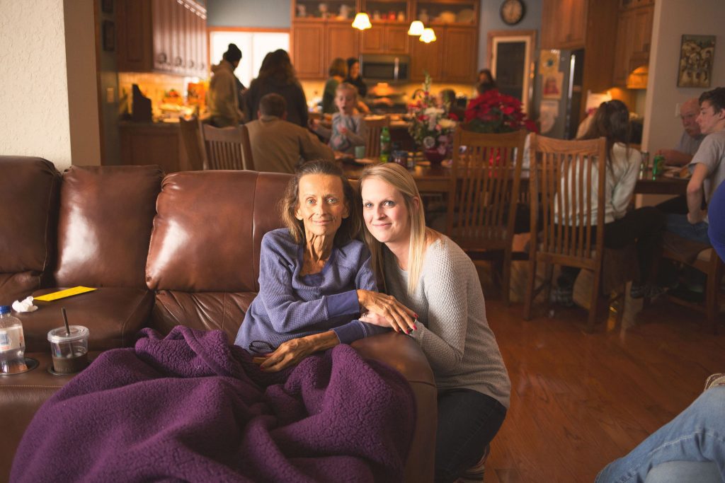 Niece kneeling beside her aunt on the couch, surrounded by family during a celebration of life gathering.