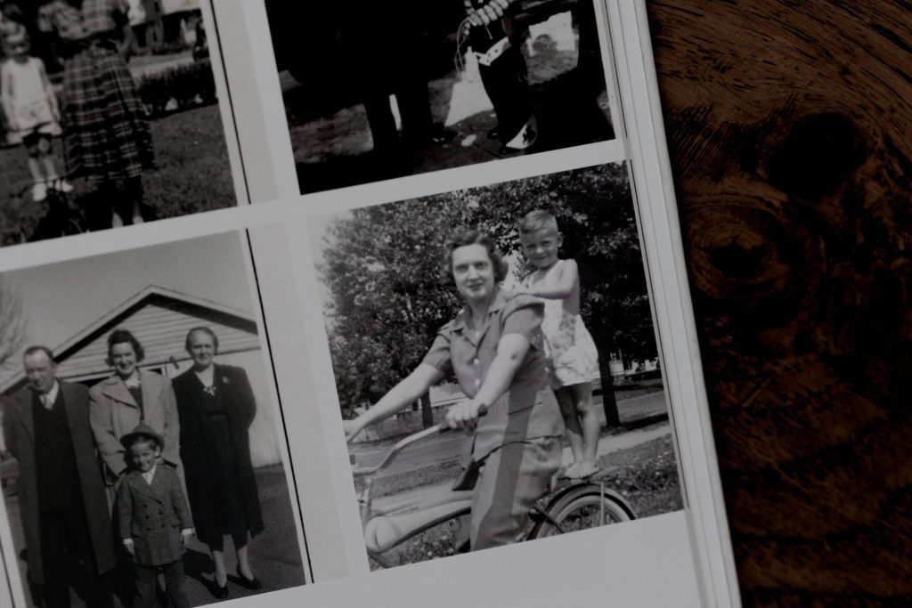 Grandmother riding bicycle with child standing on the back in black and white vintage photo.