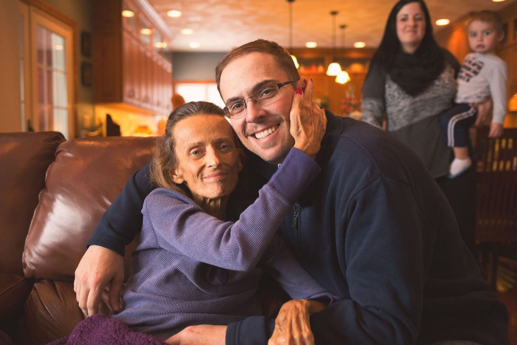 Grandmother holding her adult son close on the couch with a loving expression.