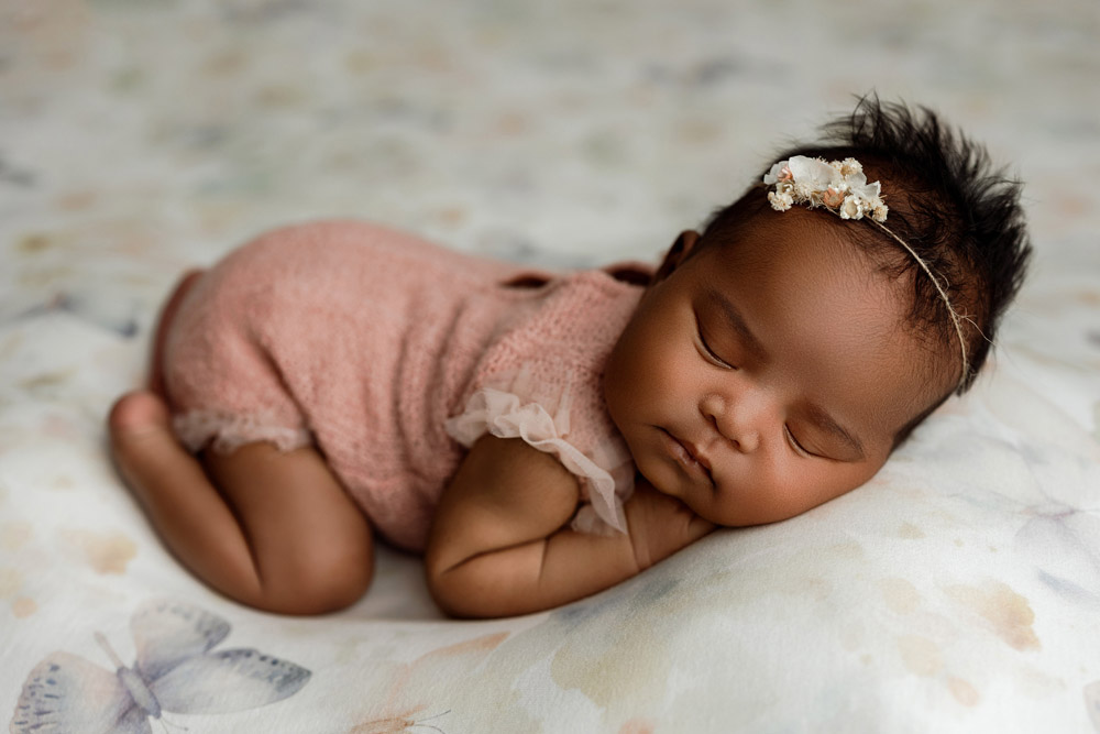 Newborn Reina posed in a side-lying position on a soft pastel butterfly blanket in Waterloo
