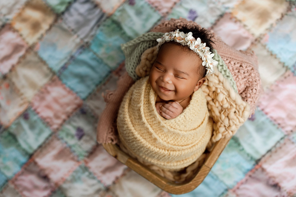 Smiling newborn wrapped in yellow knit swaddle on a quilt drop during a Cedar Falls photography session